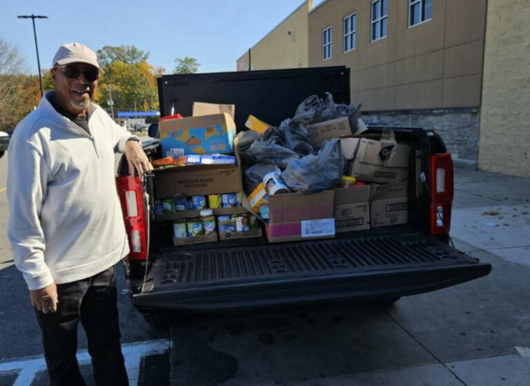 man poses with truck full of bags of food for food drive